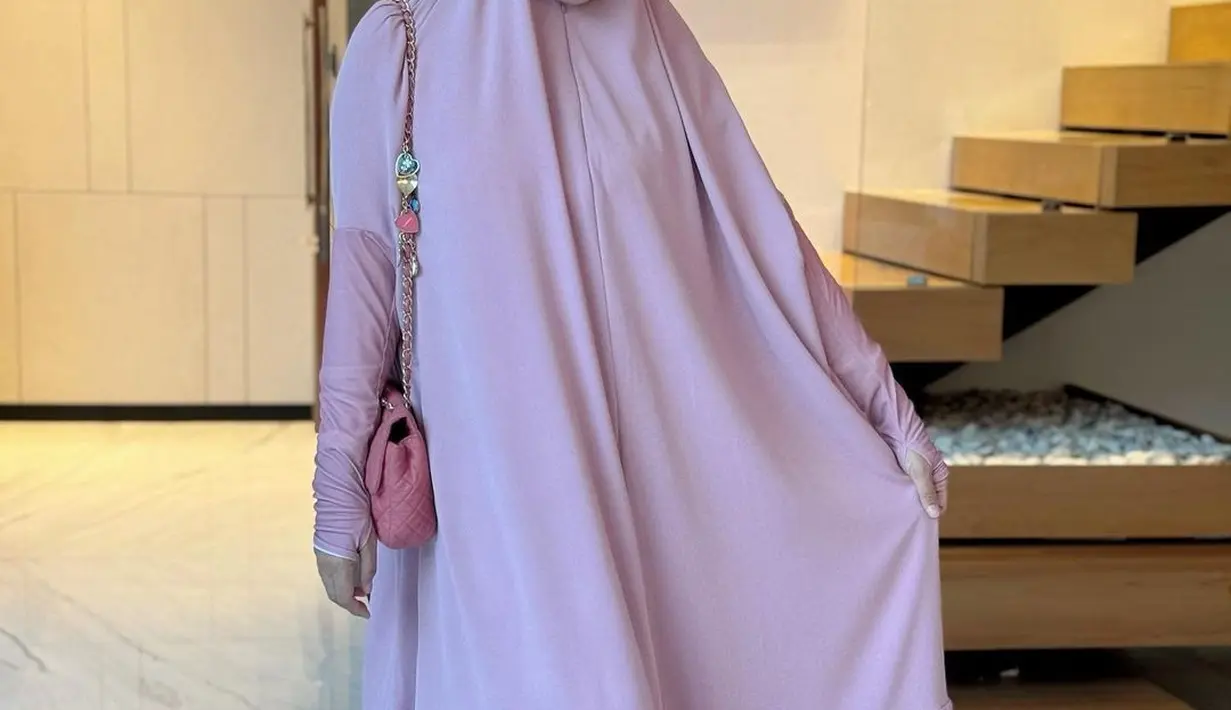 Titi Kamal kenakan busana muslim panjang pink yang menyatu dengan hijab. Penampilan cantik Titi Kamal dilengkapi dengan tas pink dari Chanel [@titi_kamall]