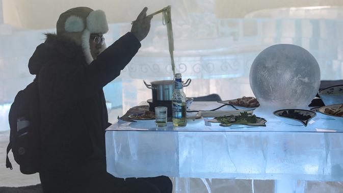 Foto yang diambil 13 Januari 2020 menunjukkan seorang pria menikmati hot pot di meja dan kursi berukir es di dalam igloo selama Festival Es dan Salju Internasional Harbin tahunan. Sementara hampir seluruh perabot di dalam restoran ini seperti meja dan kursi, terbuat dari es. (STR/AFP)