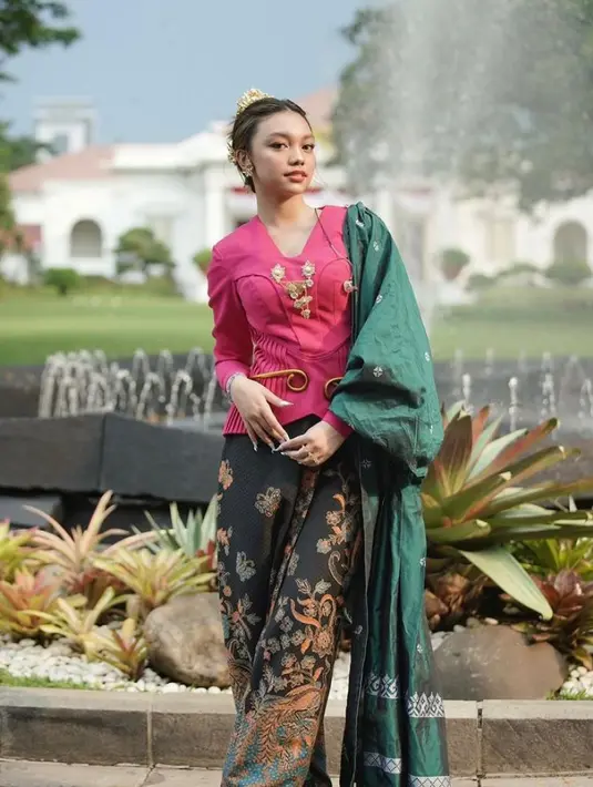 Di momen itu, ia tampil cantik mengenakan baju kurung berwarna fuschia, celana hitam bermotif batik, dan kain hijau tua yang disampirkan di bahu kirinya. Penampilannya kian sempurna dengan perhiasan adat warna emas. (Instagram/naura.ayu).
