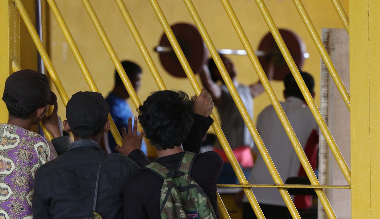 Warga menonton Atlet Angkat Besi berlatih dekat halaman Parkir Angkat Besi di Senayan, Jakarta, Senin (11/1/2016). Hal ini karena tempat Latihan dalam tahap renovasi. (Bola.com/Nicklas Hanoatubun)