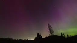 Dalam foto yang diambil dengan long exposure, orang-orang memandangi langit malam ke arah cahaya utara atau Aurora Borealis, pada hari Jumat, 10 Mei 2024, di Estacada, Oregon, Amerika Serikat. (AP Photo/Jenny Kane)