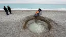 Petugas dibantu keluar dari  kawah misterius berisi air payau yang muncul di Pantai Lido, Nice, Prancis, Kamis (1/2). Pihak berwenang mengatakan, lubang yang mulai terbentuk pada Rabu itu tidak menimbulkan bahaya bagi keamanan publik. (VALERY HACHE/AFP)