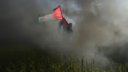 Seorang demonstran mengibarkan bendera nasional saat protes terhadap serangan militer Israel ke Kota Nablus, Tepi Barat, di sepanjang pagar perbatasan dengan Israel di sebelah timur Kota Gaza, 22 Februari 2023. Para pejabat Palestina mengatakan sejumlah warga Palestina telah terbunuh dan lebih dari seratus orang terluka dalam serangan tentara Israel yang jarang terjadi di Tepi Barat. (AP Photo/Adel Hana)