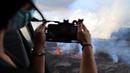 Seorang perempuan mengambil gambar gunung berapi Piton de la Fournaise yang meletus di pulau Reunion, Samudra Hindia Prancis. Gunung yang memiliki ketinggian 2632 meter ini meletus untuk kedua kalinya dalam setahun pada 22 Desember pukul 3:30 (12:30 di Paris).  (Richard BOUHET/AFP)