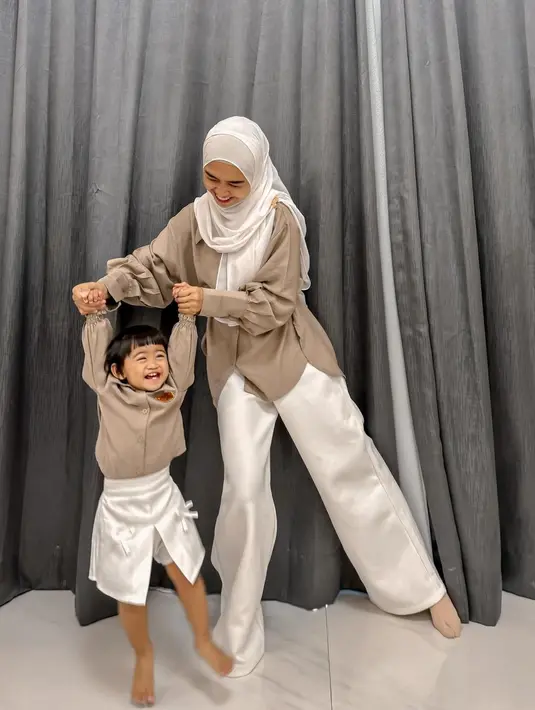 Lagi, Ria Ricis tampil kasual dengan atasan berwarna cokelat yang serasi dengan yang dikenakan sang putri, Moana. Dipadunya penampilannya dengan celana panjang putih yang serasi dengan hijabnya, sedangkan Moana mengenakan rok dengan slit di tengah dan detail pita yang manis. [Foto: Instagram/riaricis1795]