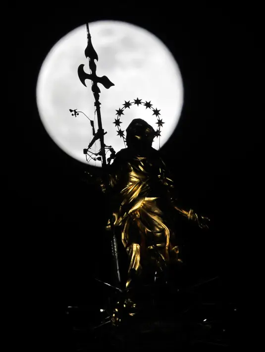Fenomena super snow moon terlihat di belakang patung Perawan Maria 'Madonnina' di atas Katedral Duomo, Milan, Italia, Selasa (19/2). Super snow moon membuat langit berada di paras paling terang sepanjang tahun. (AP Photo/Luca Bruno)