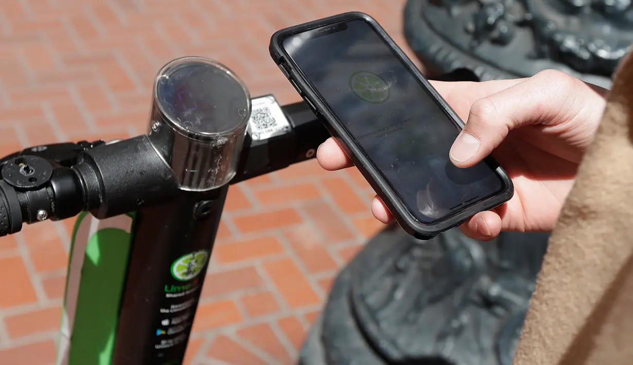 Seorang pria bernama Jack Handlery menggunakan aplikasi di ponsel pintarnya untuk menggunakan skuter bermotor di San Francisco (17/4). (AP/Jeff Chiu)