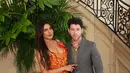 Priyanka Chopra dan Nick Jonas hadiri Dior Haute Couture dengan busana yang kontras. Priyanka kenakan v-neck dress full petal bernuansa oranye dan Nick Jonas kenakan setelan abu-abu dan kemeja kotak-kota [Dior]
