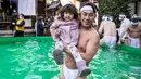 Penganut shinto dari Kuil Teppozu Inari berpose bersama seorang anak setelah mandi dengan air dingin untuk mensucikan jiwa dan tubuh mereka selama ritual Tahun Baru di Tokyo, Jepang, Minggu (9/1/2022). Laki-laki dan perempuan, tua dan muda, berbaur di dalam bak tersebut. (Philip FONG/AFP)