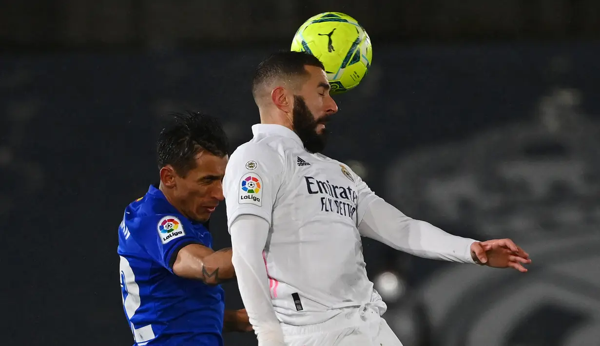 Striker Real Madrid, Karim Benzema (kanan) berduel udara dengan bek Getafe, Damian Suarez dalam laga lanjutan Liga Spanyol 2020/21 pekan ke-22 di Alfredo di Stefano Stadium, Selasa (9/2/2021). Real Madrid menang 2-0 atas Getafe. (AFP/Gabriel Bouys)