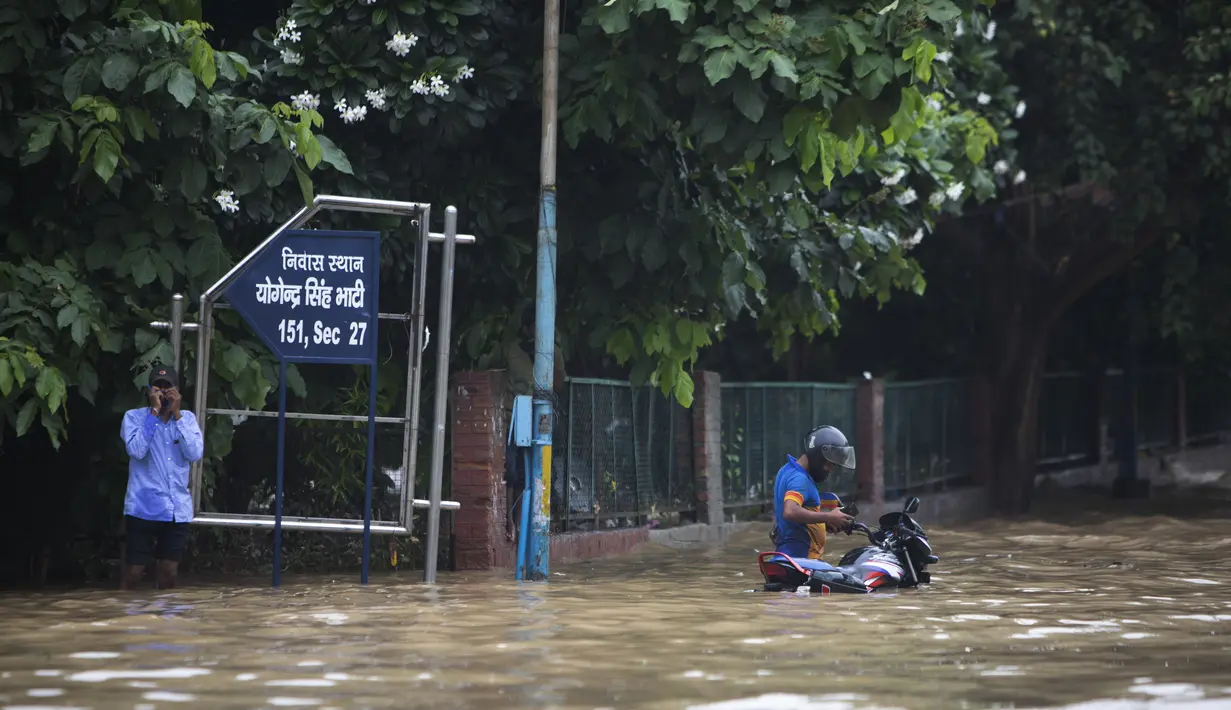 Pengendara motor  berdiri di jalan yang tergenang air setelah hujan monsun di Gurgaon di pinggiran New Delhi (19/8/2020). Jumlah korban dari banjir tahunan di seluruh Asia Selatan naik menjadi hampir 1.300. (AFP/Xavier Galiana)