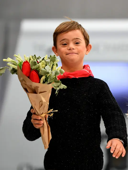 Anak laki-laki dengan down syndrome membawa buket bunga saat ambil bagian di atas catwalk pekan mode Petite Fashion Week di Madrid, 6 Oktober 2017. Tampil dalam balutan busana, mereka tampak menikmati tugasnya sebagai model. (GABRIEL BOUYS/AFP)