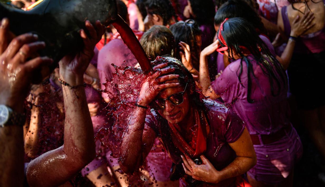 Peserta diguyur anggur merah saat ambil bagian dalam perang anggur di Haro, Spanyol utara, Sabtu (29/6/2019). Ratusan orang berpartisipasi dalam pertempuran musim panas yang terkenal ini dengan menumpahkan ribuan liter anggur merah atau wine ke tubuh peserta satu sama lain. (AP/Alvaro Barrientos)