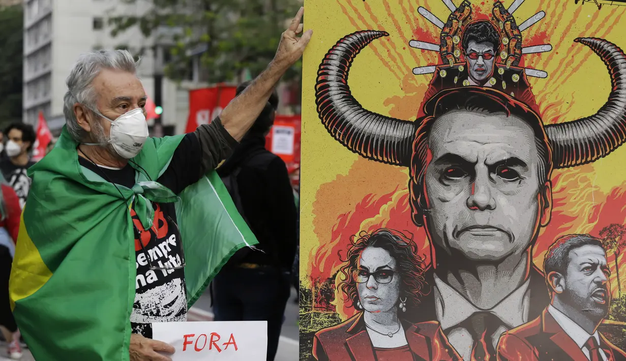 Seorang demonstran berfoto di samping spanduk yang menggambarkan Jair Bolsonaro selama protes menuntut presiden Brasil itu mengundurkan diri, di Sao Paulo, Sabtu (3/7/2021). Puluhan ribu orang turun ke jalan menuntut pemakzulan Presiden Jair Bolsonaro. (AP Photo/Nelson Antoine)