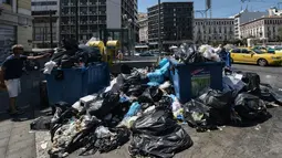 Seorang pria melemparkan kantong plastik ke tong sampah yang kepenuhan di pusat kota Athena, Kamis (22/6). Tumpukan sampah tampak menggunung di beberapa kota di Yunani setelah ribuan petugas pengumpul sampah melakukan mogok kerja. (LOUISA GOULIAMAKI/AFP)