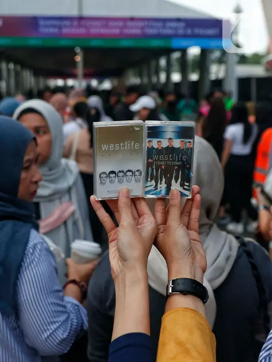 Penggemar Westlife menunjukkan album dalam bentuk fisik kaset tape saat tiba untuk menonton konser bertajuk 'The Wild Dreams Tour 2023' di kawasan Stadion Utama Gelora Bung Karno Sabtu (11/2/2023). Konser musik Westlife akan membawakan semua lagu hits mereka seperti Swear It Again, Flying Without Wings, dan World of our own serta lagu-lagu andalan dari album terbaru mereka yang bertajuk Wild Dreams. (Liputan6.com/Angga Yuniar)