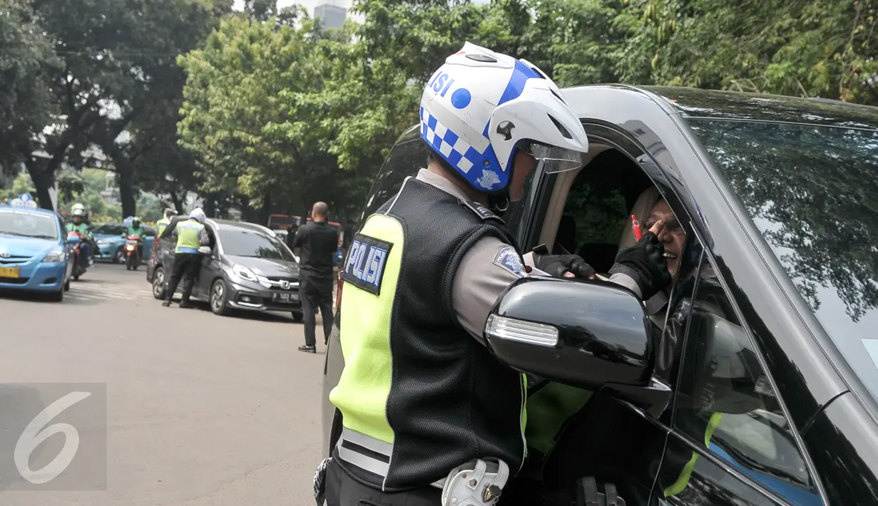 Petugas melakukan tilang di tempat ke salah satu pelanggar aturan pembatasan kendaraan sistem ganjil genap di kawasan Sudirman, Jakarta, Selasa (30/8). Hari ini resmi diberlakukan denda bagi pelanggar aturan sistem ganjil genap (Liputan6.com/Yoppy Renato)