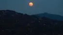 Bulan Purnama Super Pink terlihat di atas lingkungan Petare di Caracas, Venezuela, pada Senin (26/4/2021). Super Pink Moon merupakan fenomena alam ketika posisi bulan purnama berada terdekat dengan bumi. (Federico Parra / AFP)