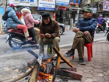 Orang-orang menghangatkan diri dengan membakar kayu pada hari musim dingin di Hanoi, Vietnam, Jumat (8/1/2021). Vietnam tahun ini diperkirakan mengalami musim dingin yang lebih dingin dari biasanya ketika suhu permukaan laut Samudra Pasifik turun, membentuk fenomena La Nina. (Nhac NGUYEN/AFP)