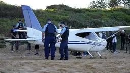 Polisi berdiri di dekat sebuah pesawat ringan yang melakukan pendaratan darurat di sebuah pantai di Sydney, Rabu (26/5/2021). Pesawat kategori rekreasi itu mendarat selamat di pantai Sydney dengan tiga orang di dalamnya termasuk seorang bayi setelah mengalami kerusakan mesin. (AP Photo/Mark Baker)