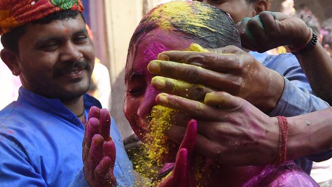 Sejumlah pria mengolesi bubuk warna pada wajah seorang gadis saat merayakan festival Holi di sebuah kuil di desa Nandgaon, Uttar Pradesh, 5 Maret 2020. Festival Holi diselenggarakan pada awal musim semi yaitu pada akhir Februari hingga Maret, tepatnya sesudah bulan purnama. (Money SHARMA/AFP)