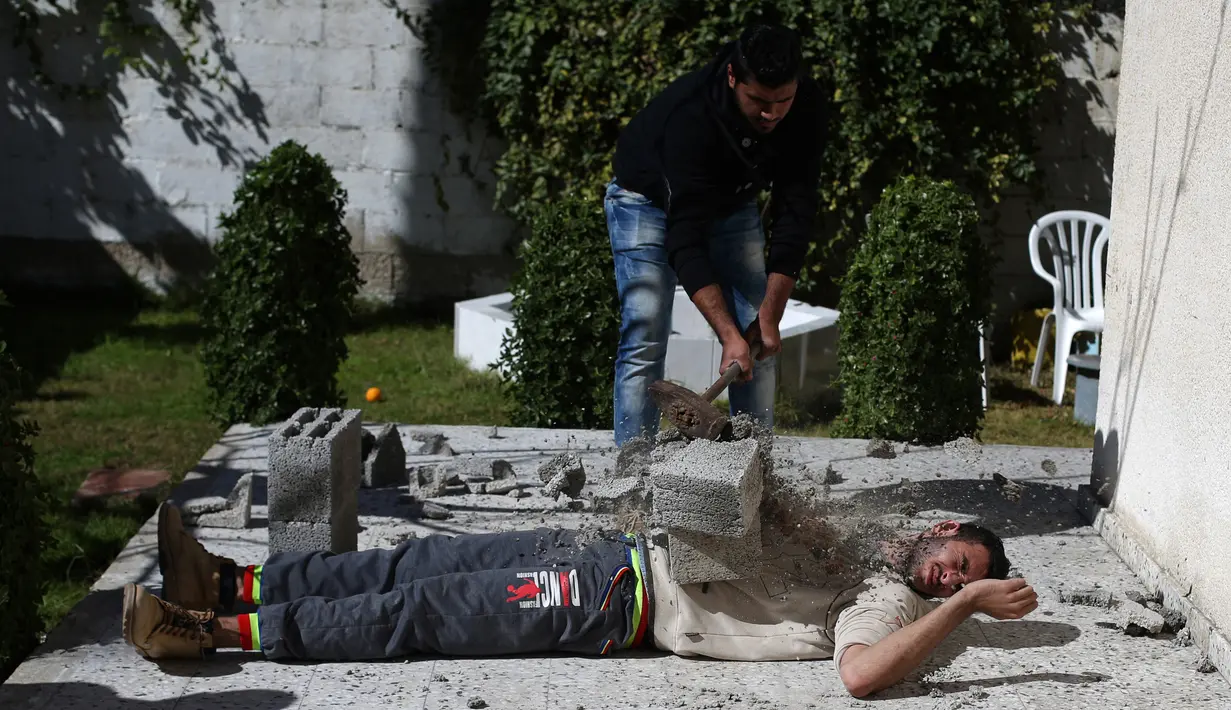 Mohamed Barka, pria yang dijuluki "Super Hero" asal Palestina menjadikan tubuhnya sebagai bantalan untuk menghancurkan batu bata beton dalam aksinya di Deir Al-Balah, Gaza Tengah, Kamis (4/2). (MOHAMMED ABED/AFP)