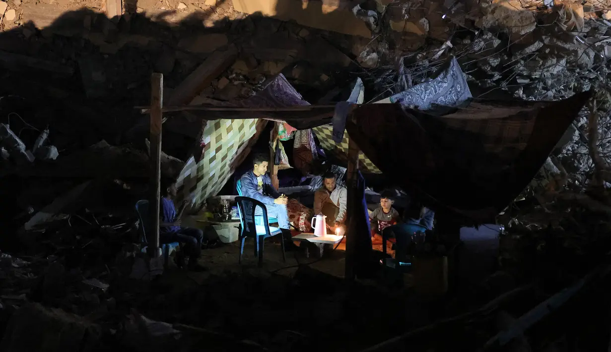 Warga Palestina duduk di tenda yang didirikan di atas reruntuhan bangunan yang hancur dalam serangan udara Israel di Kota Gaza (24/5/2021). Menyusul gencatan senjata yang dicapai setelah perang 11 hari antara Israel dan Hamas, Warga Palestina mendirikan tenda di reruntuhan. (AFP/Mohamed Abed)