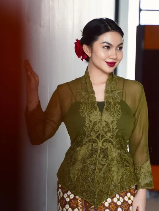 Penampilan memukau Ariel Tatum pakai kebaya hijau dan kain batik cokelat muda. Ia tata rambutnya dengan sanggul rendah, yang diberi aksesori bunga merah dan pulasan lipstik merah yang serasi. [Foto: Instagram/arieltatum]