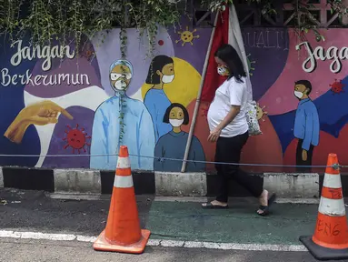 Warga yang mengenakan masker berjalan melintasi mural berisi imbauan terkait COVID-19 di Menteng, Jakarta, Kamis (7/10/2021). Menteri Kesehatan Budi Gunadi mengatakan perihal pandemi menjadi endemi dengan menyebutkan empat langkah yang dipersiapkan. (Liputan6.com/Johan Tallo)