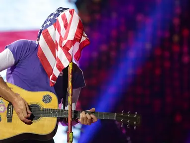 Vokalis grup band Coldplay, Chris Martin menutupi wajahnya dengan bendera Amerika Serikat sambil memainkan gitarnya saat menghibur para penonton di Lapangan FedEx di Landover, Md, AS (6/8). (Photo by Brent N. Clarke/Invision/AP)