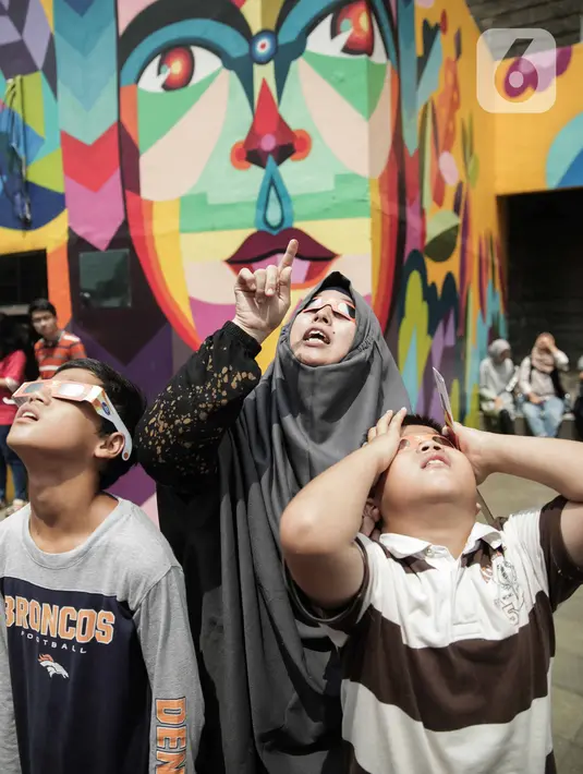 Pengunjung mengamati gerhana matahari cincin memakai kacamata khusus di Planetarium Taman Ismail Marzuki, Jakarta, Kamis (26/12/2019). Planetarium menyediakan sekitar 10 teleskop dan kacamata khusus agar pengunjung bisa menyaksikan gerhana matahari cincin dengan aman. (Liputan6.com/Faizal Fanani)
