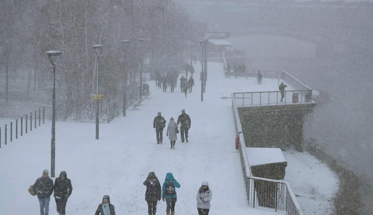 Pejalan kaki berjalan di tepi sungai Thames saat hujan salju melanda London (27/2). Cuaca ekstrem yang melanda sebagian wilayah Eropa menyebabkan warga dan wisatawan mengalami sakit dan beberapa meninggal akibat kedinginan. (AFP Photo/Daniel Leal-Olivas)