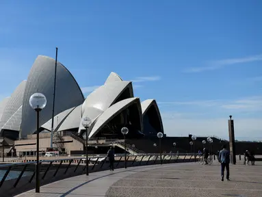 Orang-orang berjalan melalui halaman depan Gedung Opera Sydney yang sepi saat lockdown minggu kedua untuk meredam gejolak varian Delta Covid-19, Selasa (6/7/2021). PM Gladys Berejiklian mengatakan pihaknya akan menentukan nasib lockdown yang sedang diberlakukan di Sydney. (Bianca De Marchi/AFP)