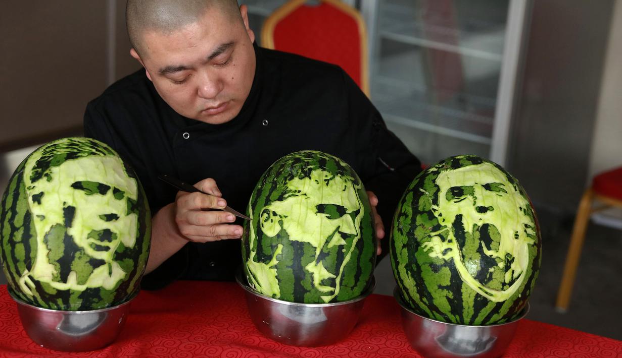 Seorang guru sekolah menengah mengukir wajah pemain sepak bola Prancis, Antoine Griezmann (tengah) pada buah semangka di Shenyang, Provinsi Liaoning, China, Senin (9/7). (AFP)