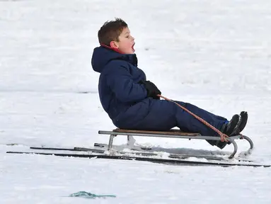 Seorang anak bermain kereta luncur selama hujan salju di taman Dunorlan di Tunbridge Wells, Inggris (27/2). Cuaca dingin di Siberia yang dijuluki "The Beast from the East" membuat suhu di sebagian Eropa menurun. (AFP Photo/Ben Stansall)