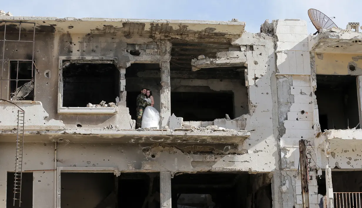 Sepasang pengantin, Nada Merhi (18) dan tentara Suriah, Hassan Youssef (27), berpose di tengah bangunan yang hancur akibat perang saat menjalani sesi foto pernikahan di kota Homs, 5 Februari 2016. (JOSEPH EID/AFP)