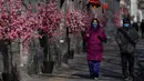Warga mengenakan masker untuk membantu melindungi dari virus corona berjalan melewati dekorasi bunga dan lentera untuk Tahun Baru Imlek mendatang di Beijing, Kamis (27/1/2022). (AP Photo/Andy Wong)