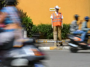 Pengendara melintasi manekin pria berseragam polisi lalu lintas di persimpangan jalan di Bangalore, India, Senin (16/12/2019). Polisi manekin itu diharapkan bisa mengelabui pengemudi yang akan mengiranya sebagai polisi asli sehingga mengurungkan niat melanggar lalu lintas. (Manjunath KIRAN / AFP)