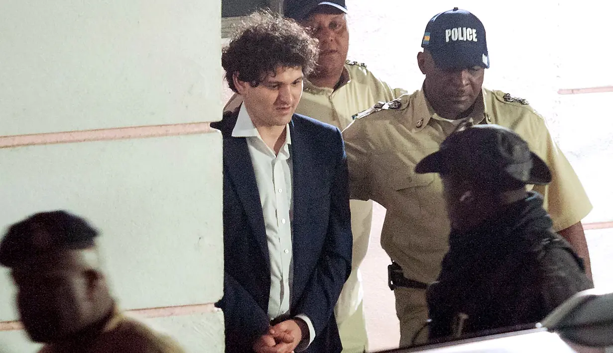 Pendiri FTX Sam Bankman-Fried (kedua kiri) dibawa pergi dengan tangan diborgol oleh petugas Kepolisian Kerajaan Bahama di Nassau, Bahamas, 13 Desember 2022. Bankman-Fried dijadwalkan akan bersaksi di hadapan Kongres di Komite Jasa Keuangan DPR AS, namun hal itu batal dilakukan karena eks CEO FTX itu telah ditahan berdasarkan dakwaan tertutup. (Mario Duncanson/AFP)