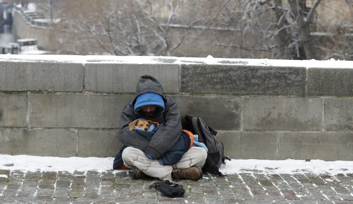 Seorang pengemis menggendong anjingnya di Jembatan Charles abad pertengahan setelah hujan salju pertama di Praha, Republik Ceko (3/12/2020). (AP Photo / Petr David Josek)