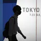 Seorang pria yang mengenakan masker pelindung untuk membantu mengekang penyebaran virus corona berjalan di depan logo Olimpiade Tokyo 2020 di Tokyo, Selasa (22/6/2021). Ibu kota Jepang mengkonfirmasi lebih dari 430 kasus virus corona baru pada hari Selasa. (AP Photo/Eugene Hoshiko)