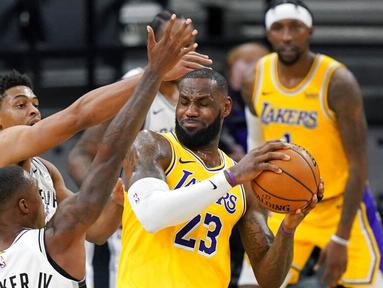 Pebasket Los Angeles Lakers, LeBron James, berebut bola dengan pebasket San Antonio Spurs, Lonnie Walker dan Keldon Johnson pada laga NBA di AT&T Center, Kamis (31/12/2020). LA Lakers menang dengan skor 121-107. (AP/Eric Gay)