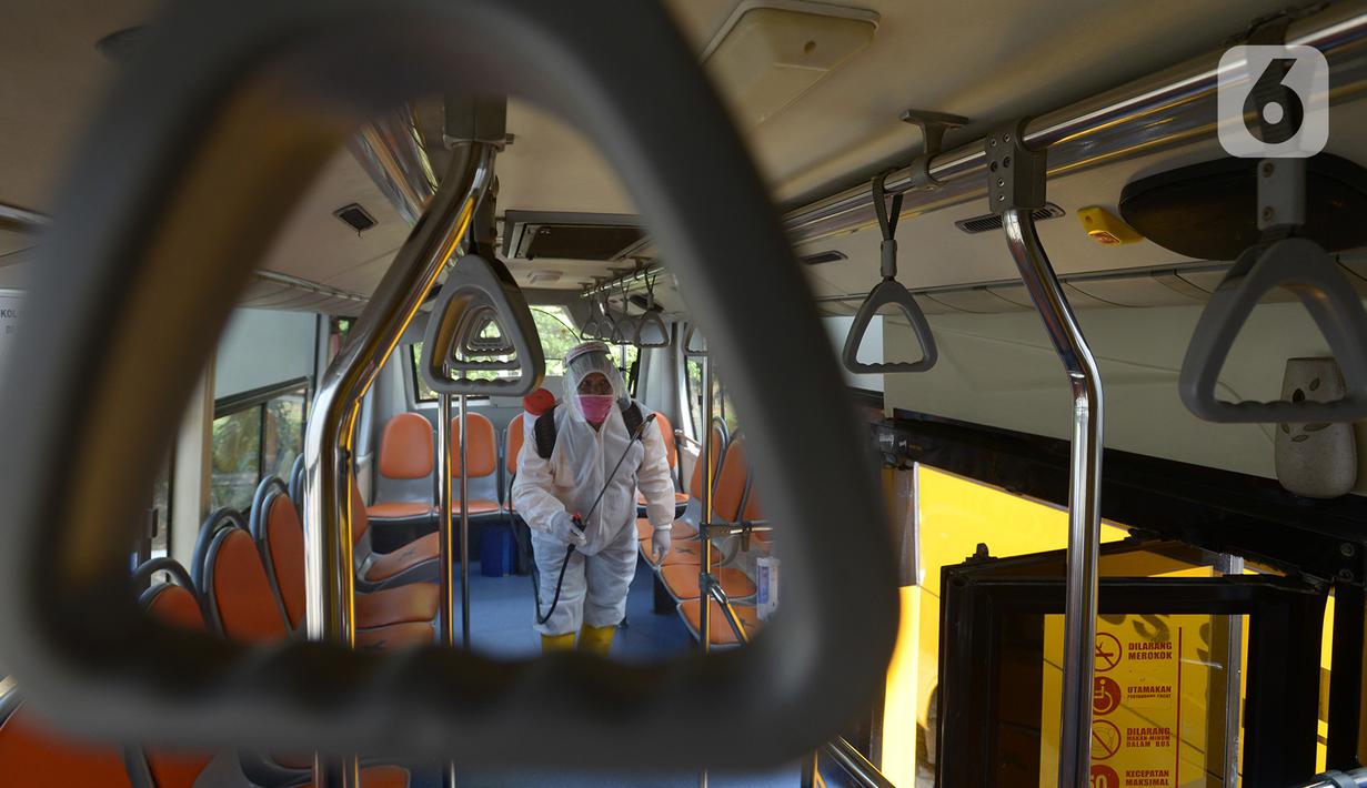 Petugas ber-APD menyemprotkan disinfektan pada bus sekolah di Posko Gabungan PSBB dan Gakplin Protkes, Puskesmas Jatinegara, Jakarta, (22/9/2020). Sejumlah unit bus sekolah kini dialihfungsikan menjadi kendaraan untuk mengantar pasien Covid-19 berstatus OTG menuju Wisma Atlet. (merdeka.com/Imam Buho
