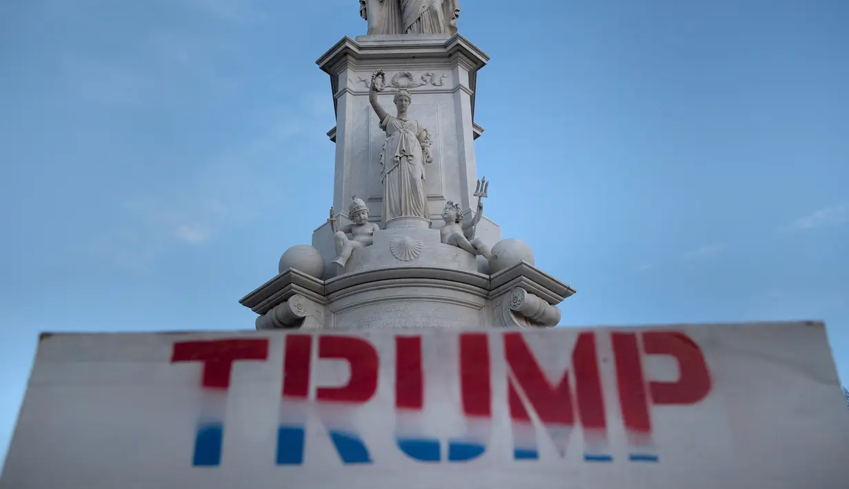 Tanda pro-Trump terlihat ditinggalkan dekat patung di Capitol Hill AS sehari setelah massa menerobos masuk ke Gedung Capitol di Washington, DC. Kamis (7/1/2021). Peristiwa penyerbuan di gedung Capitol Hill AS dilakukan oleh massa pendukung Donald Trump pada 6 Januari. (Brendan Smialowski/AFP)