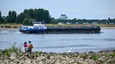 <p>Sebuah kapal pedalaman berlayar di Rhine saat orang-orang berdiri di pantai di tepi sungai yang sebagian mengering di Duesseldorf, Jerman barat (25/7/2022). Keringnya sungah Rhine akibat Eropa mengalami gelombang panas. (AFP/Photo/Ina Fassbender)</p>
