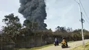 Pengendara motor melewati kepulan asap tebal dari kebakaran yang melanda Kilang Pertamina Balongan di Indramayu, Jawa Barat, Indonesia, Senin (29/3/2021). Tangki T-301G Kilang Balongan milik Pertamina terbakar pada 29 Maret 2021 mulai sekitar pukul 00.45 dini hari. (AP Photo)