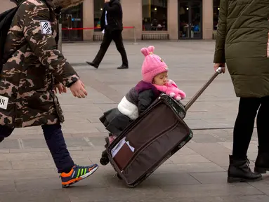 Seorang anak berada di koper di luar Stasiun Kereta Api Beijing, China (9/2). Sambut perayaan Imlek 2018, Jutaan warga China mulai memenuhi stasiun, bandara dan jalan yang diperkirakan akan dimulai akhir pekan ini. (AP Photo / Mark Schiefelbein)