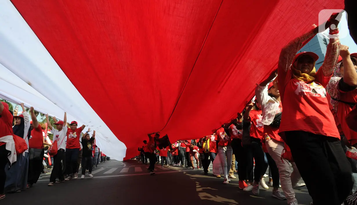 Relawan Jokowi-Ma'ruf Amin membawa bendera raksasa sepanjang sekitar 200 meter saat menyambut pelantikan Presiden-Wapres terpilih periode 2019-2024 di sekitar Patung Kuda, Jakarta, Minggu (20/10/2019). (merdeka.com/Arie Basuki)
