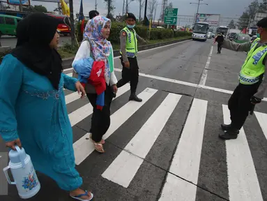 Petugas kepolisian membantu warga menyeberang jalan di Perempatan Cileunyi, Jawa Barat, Jumat (1/7). Mulai banyaknya kendaraan pemudik membuat petugas kepolisian membantu pejalan kaki yang ingin menyeberang. (Liputan6.com/Immanuel Antonius) 