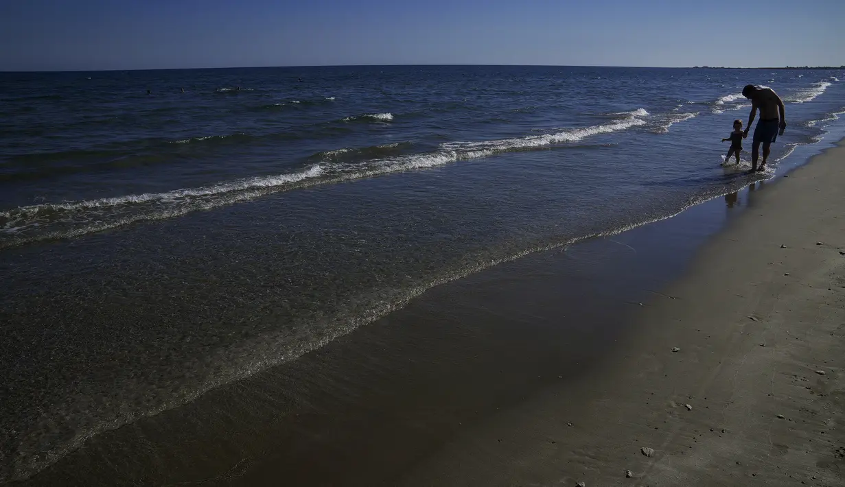 Seorang ayah dengan anaknya berjalan melintasi laut saat mereka menikmati cuaca hangat di pantai Makenzi di selatan kota Larnaca, Siprus, Senin (8/11/2021). Siprus mengalami cuaca seperti musim panas dalam beberapa hari terakhir dengan suhu tinggi yang tidak sesuai musim dan langit cerah. (AP Photo/